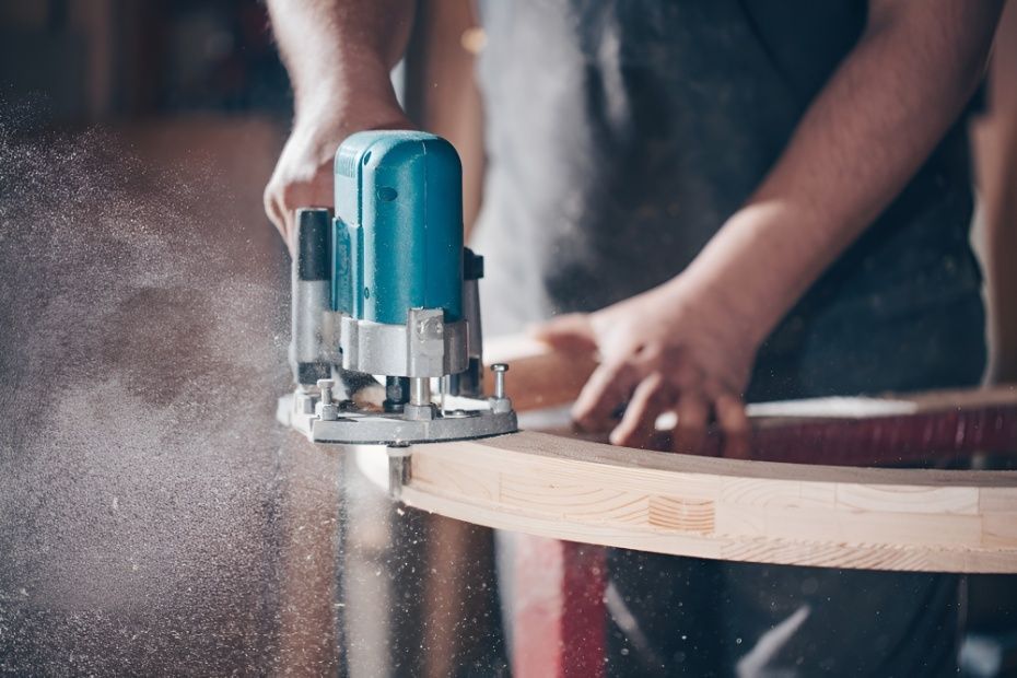 A Man is Using a Router to Cut a Piece of Wood — Mick's Carpentry & Maintenance In Palm Cove, QLD