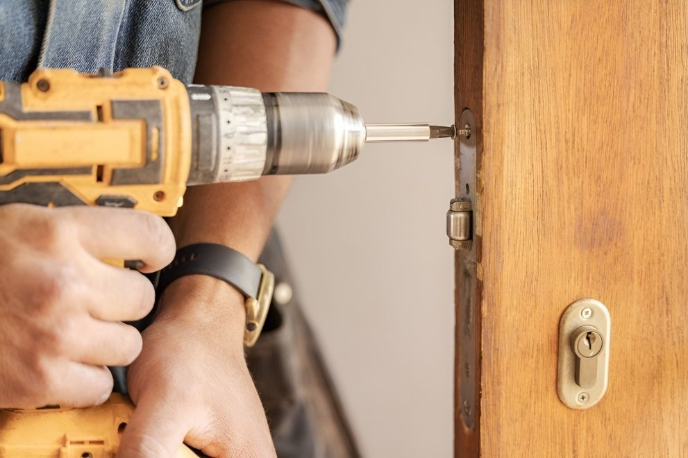 A Man is Using a Drill to Fix a Door Lock — Mick's Carpentry & Maintenance In Machans Beach, QLD