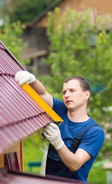 A Man is Installing a Metal Roof on a House — Mick's Carpentry & Maintenance In Machans Beach, QLD
