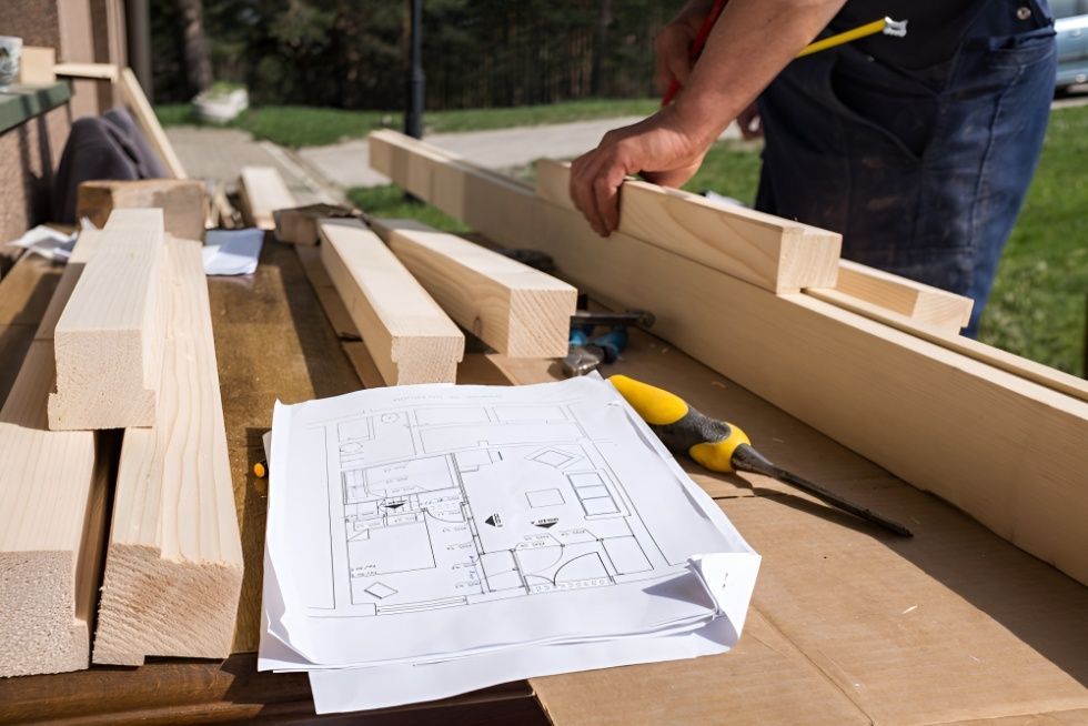 A Man is Measuring a Piece of Wood on a Table — Mick's Carpentry & Maintenance In Tablelands, QLD