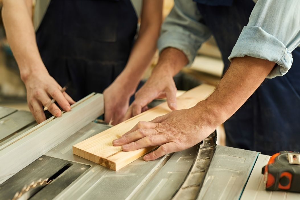 A Man and a Woman Are Cutting a Piece of Wood on a Table Saw— Mick's Carpentry & Maintenance In Tablelands, QLD