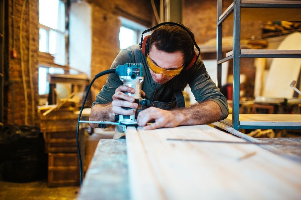 A Man is Using a Router on a Piece of Wood in a Workshop — Mick's Carpentry & Maintenance In Tablelands, QLD