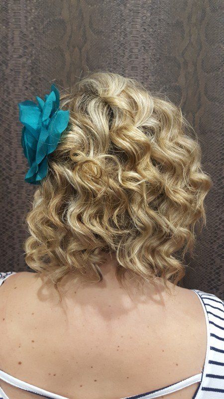 Una mujer con cabello rubio y rizado lleva una flor azul en el pelo.