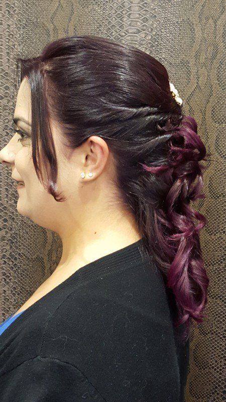 Una mujer con cabello morado lleva una camisa negra y tiene el cabello recogido en una cola de caballo.