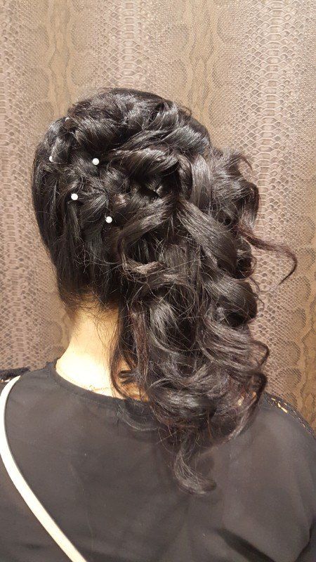 Una mujer con cabello largo y negro lleva una cola de caballo trenzada con perlas.