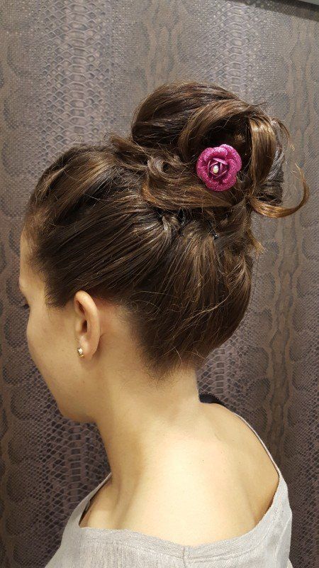 Una mujer lleva un moño con una flor rosa en el pelo.