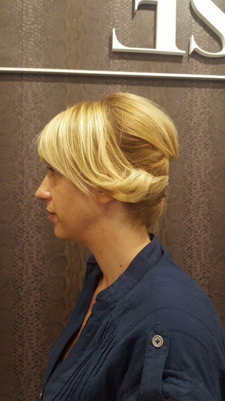 Una mujer con cabello rubio lleva una camisa azul y tiene el cabello recogido en un moño.