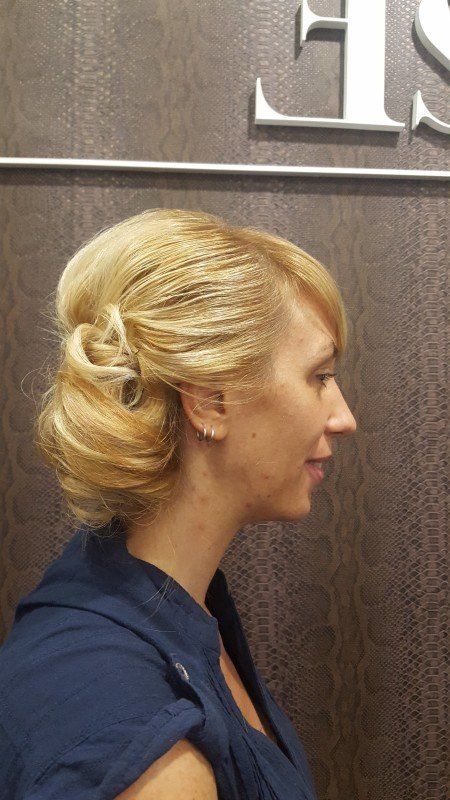 Una mujer con cabello rubio recogido en un moño está parada frente a un cartel.