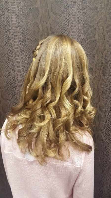 Una mujer con cabello rubio lleva un suéter rosa y tiene el cabello recogido en una trenza.