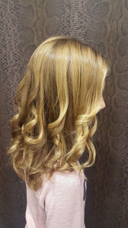 Una niña con cabello rubio y rizado lleva un suéter rosa.