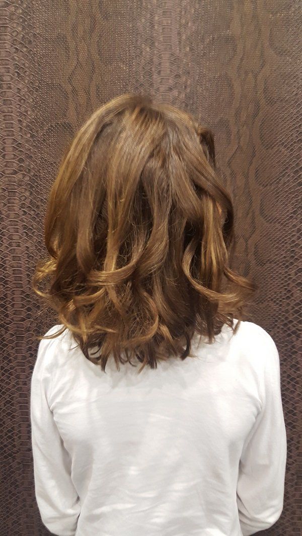 Una niña con cabello corto y castaño viste una camisa blanca y está parada frente a una pared marrón.