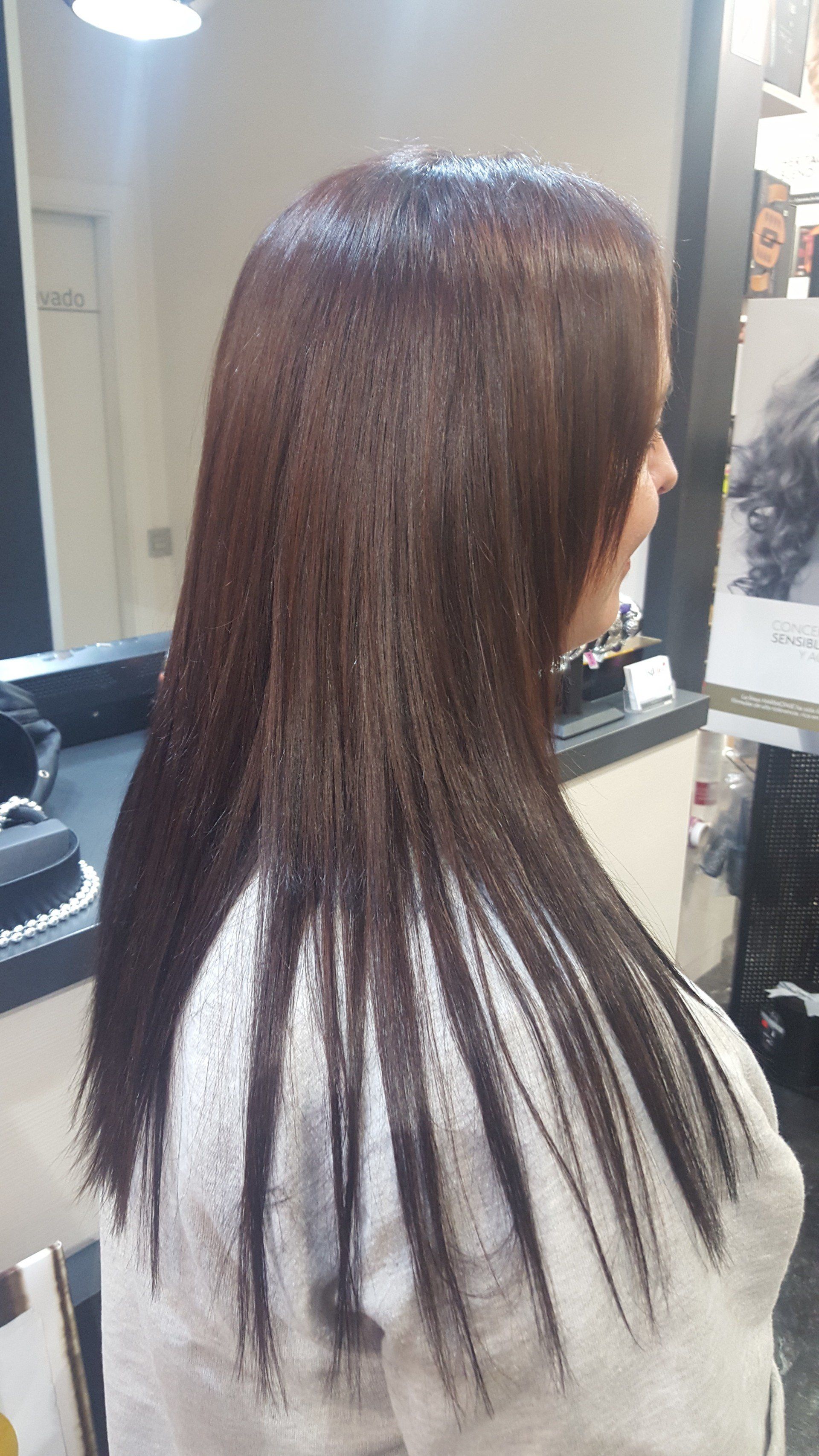 Una mujer con cabello largo y castaño está sentada frente a un espejo en un salón.