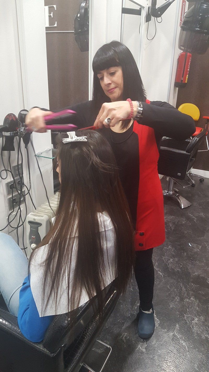 Una mujer está alisando el cabello de otra mujer en un salón.