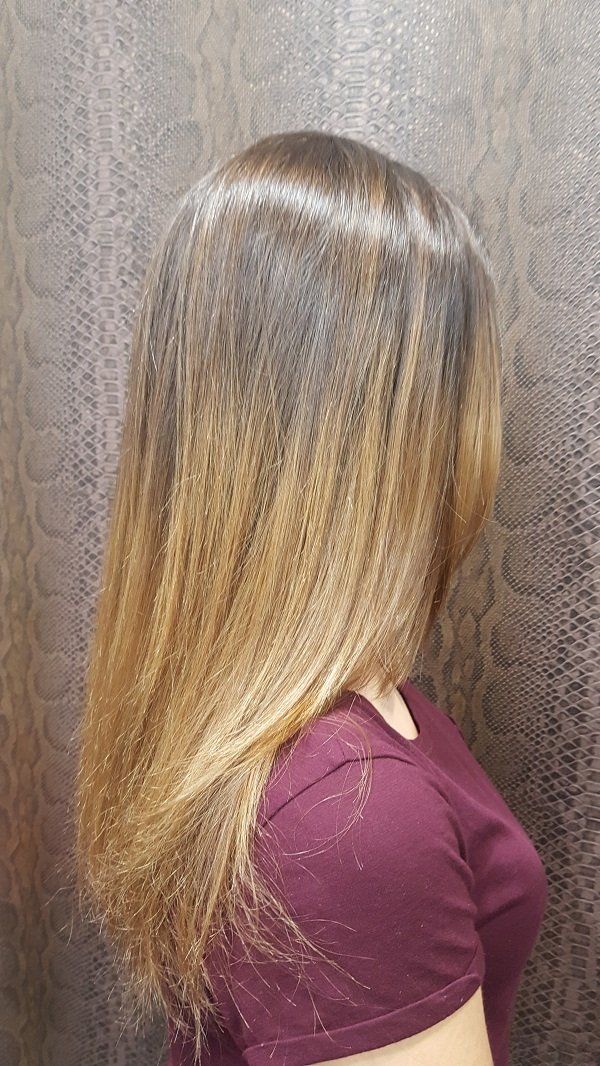 Una mujer con cabello largo lleva una camisa morada y está parada frente a una pared.