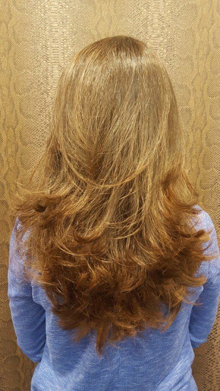 Una mujer con cabello largo y rubio lleva un suéter azul y está parada frente a una pared.