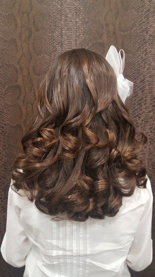 Una mujer con cabello largo y castaño lleva una camisa blanca y una flor en el pelo.