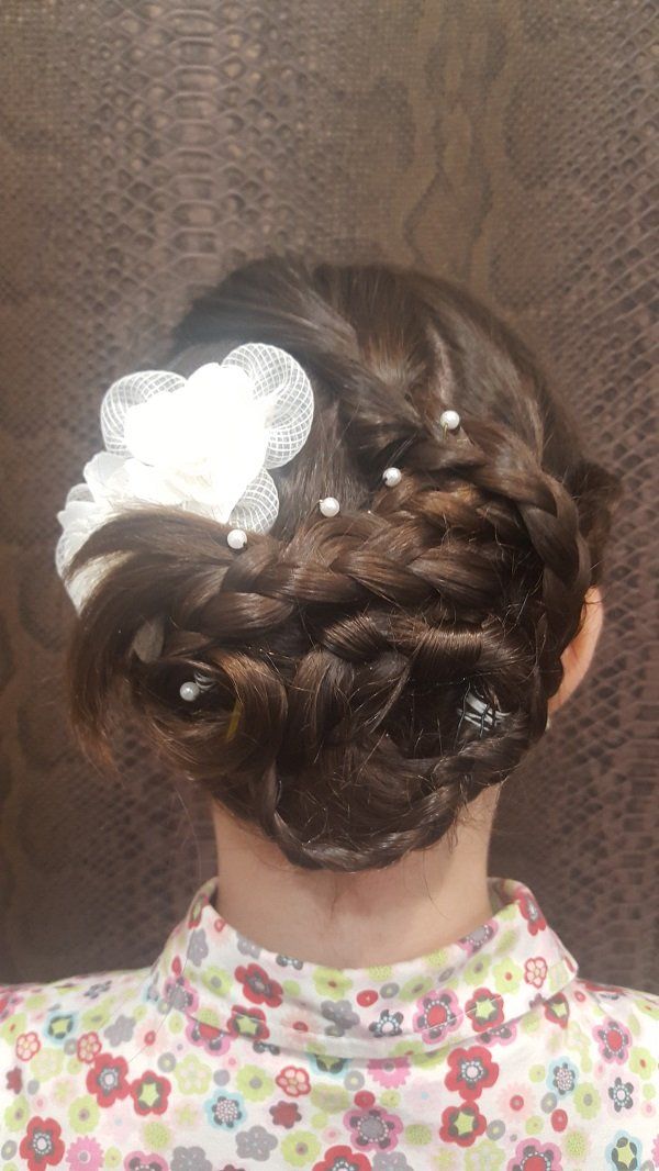 Una mujer lleva un moño trenzado con una flor en el pelo.