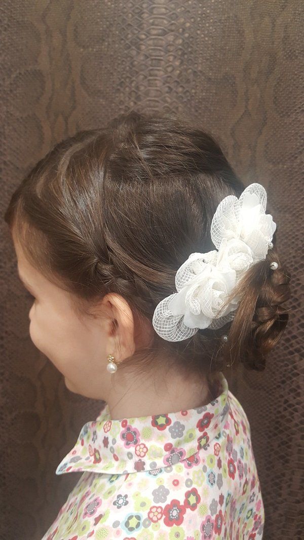 Una niña lleva un moño con una flor en el pelo.