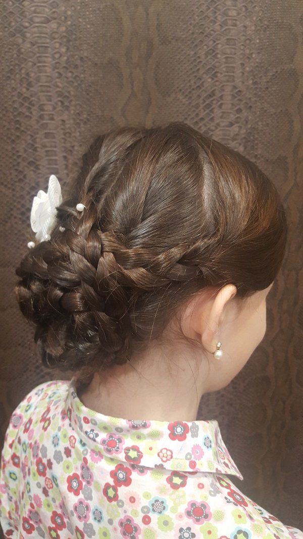 Una niña lleva un moño trenzado con una flor en el pelo.