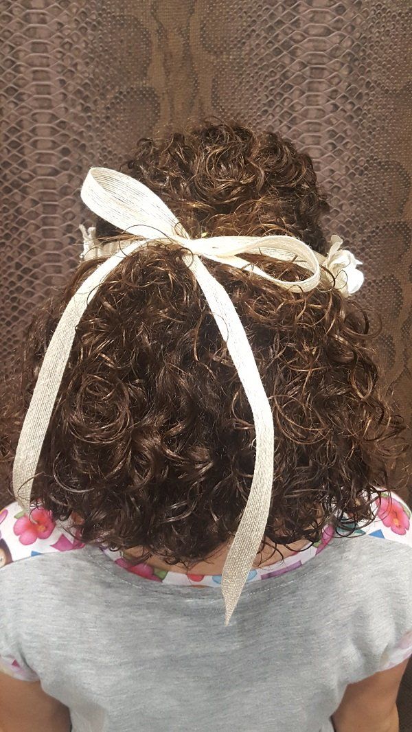 Una niña con cabello rizado lleva un lazo blanco en el pelo.