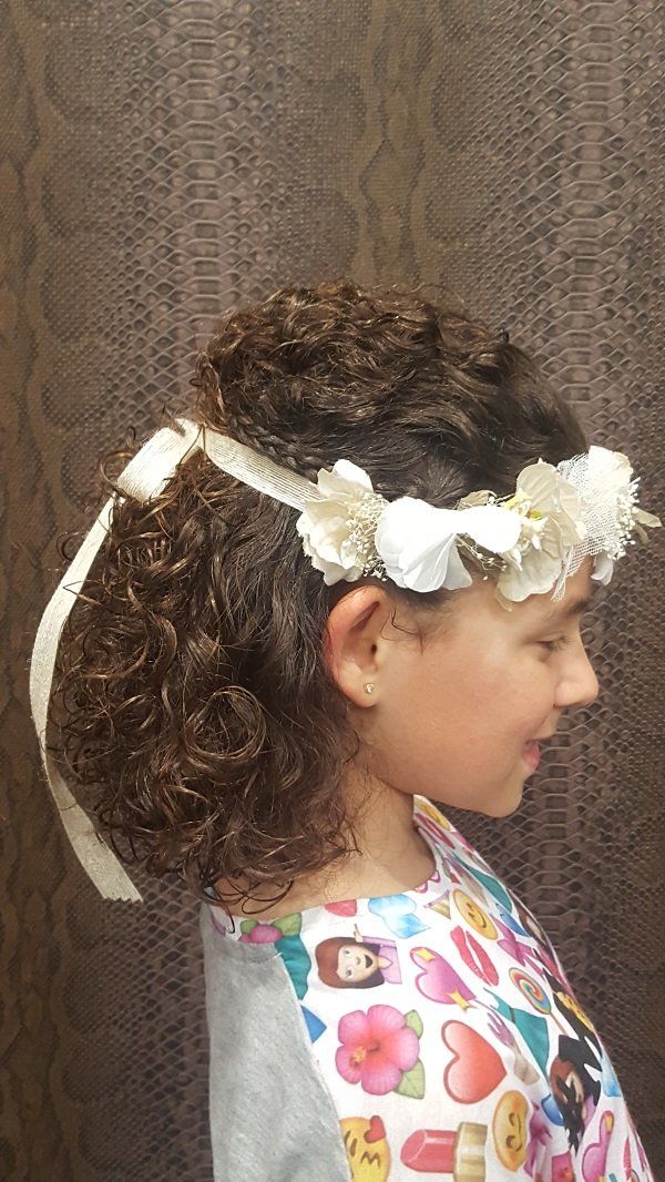 Una niña con cabello rizado lleva una corona de flores en el pelo.