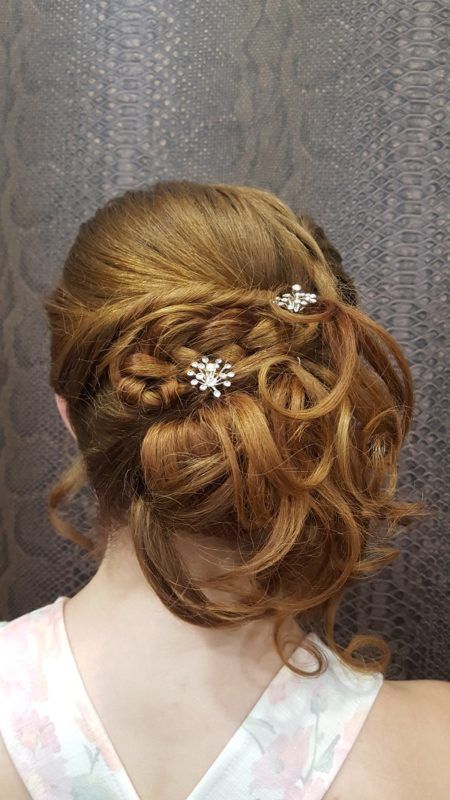 Una mujer con cabello rojo lleva un moño trenzado con una flor en el pelo.
