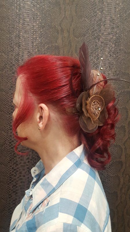 Una mujer con cabello rojo lleva una camisa a cuadros y tiene una flor en el cabello.