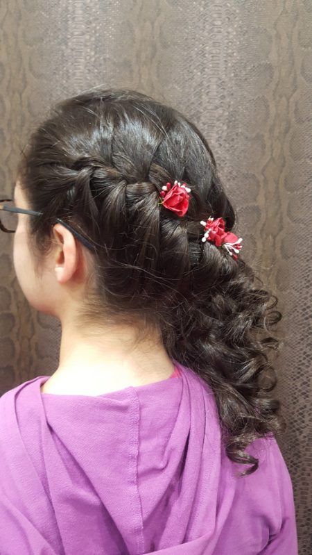 Una mujer con una sudadera con capucha morada lleva una cola de caballo trenzada con flores rojas en el pelo.