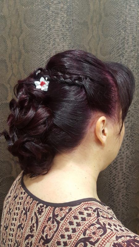 Una mujer lleva un moño trenzado con una flor en el pelo.