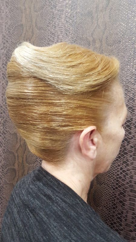 Una mujer con cabello rubio recogido en un moño está parada frente a una pared.