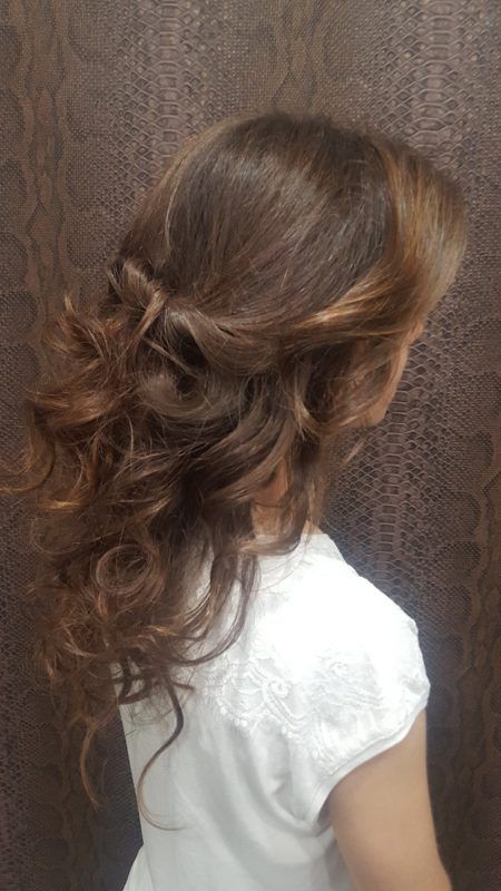 Una niña con cabello largo y castaño lleva un vestido blanco y tiene el cabello recogido mitad arriba y mitad abajo.