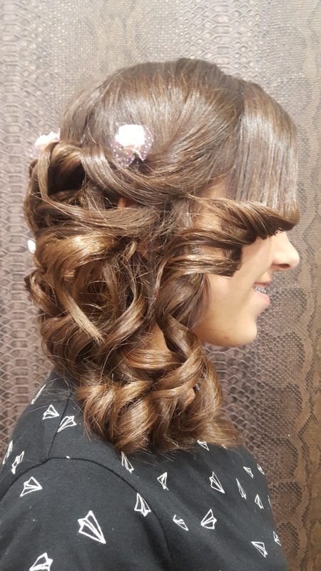 Una mujer con cabello rizado lleva una camisa negra y tiene una flor en el cabello.