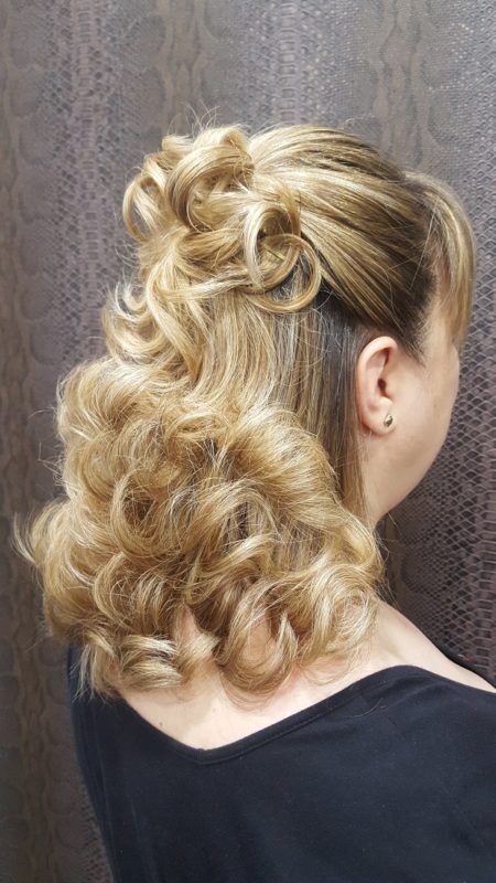 Una mujer con cabello rubio lleva una camisa negra y tiene el cabello recogido mitad arriba y mitad abajo.