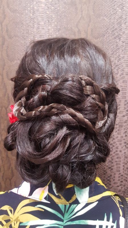 Una mujer lleva un moño trenzado con una flor roja en el pelo.