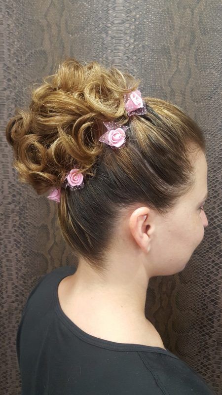 Una mujer lleva un moño con flores rosas en el pelo.