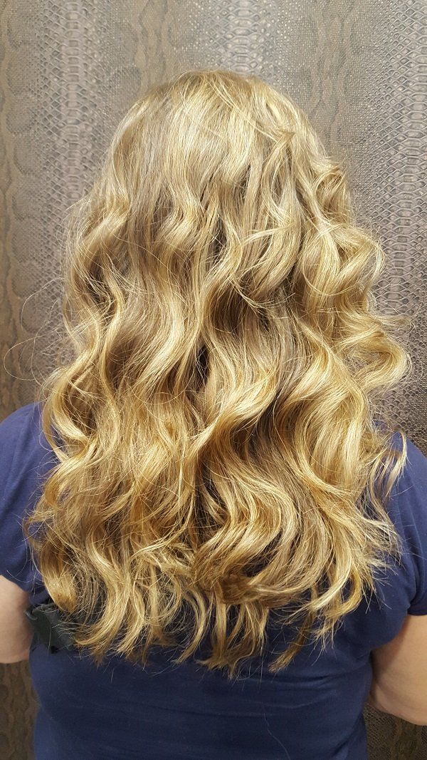 Una mujer con cabello largo, rubio y rizado lleva una camisa azul.