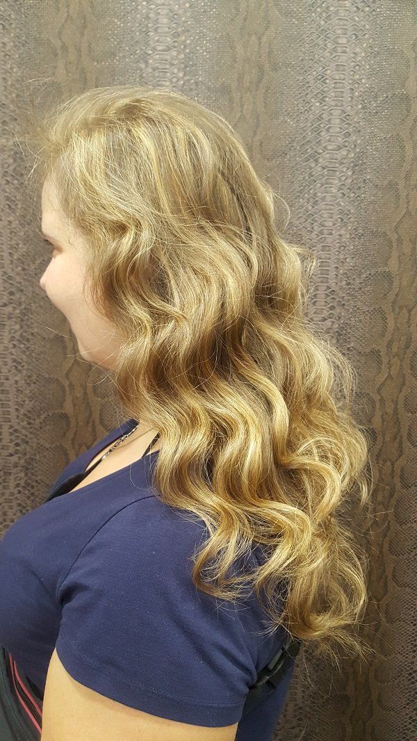 Una mujer con cabello largo, rubio y rizado lleva una camisa azul.