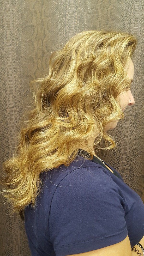 Una mujer con cabello largo, rubio y rizado lleva una camisa azul.