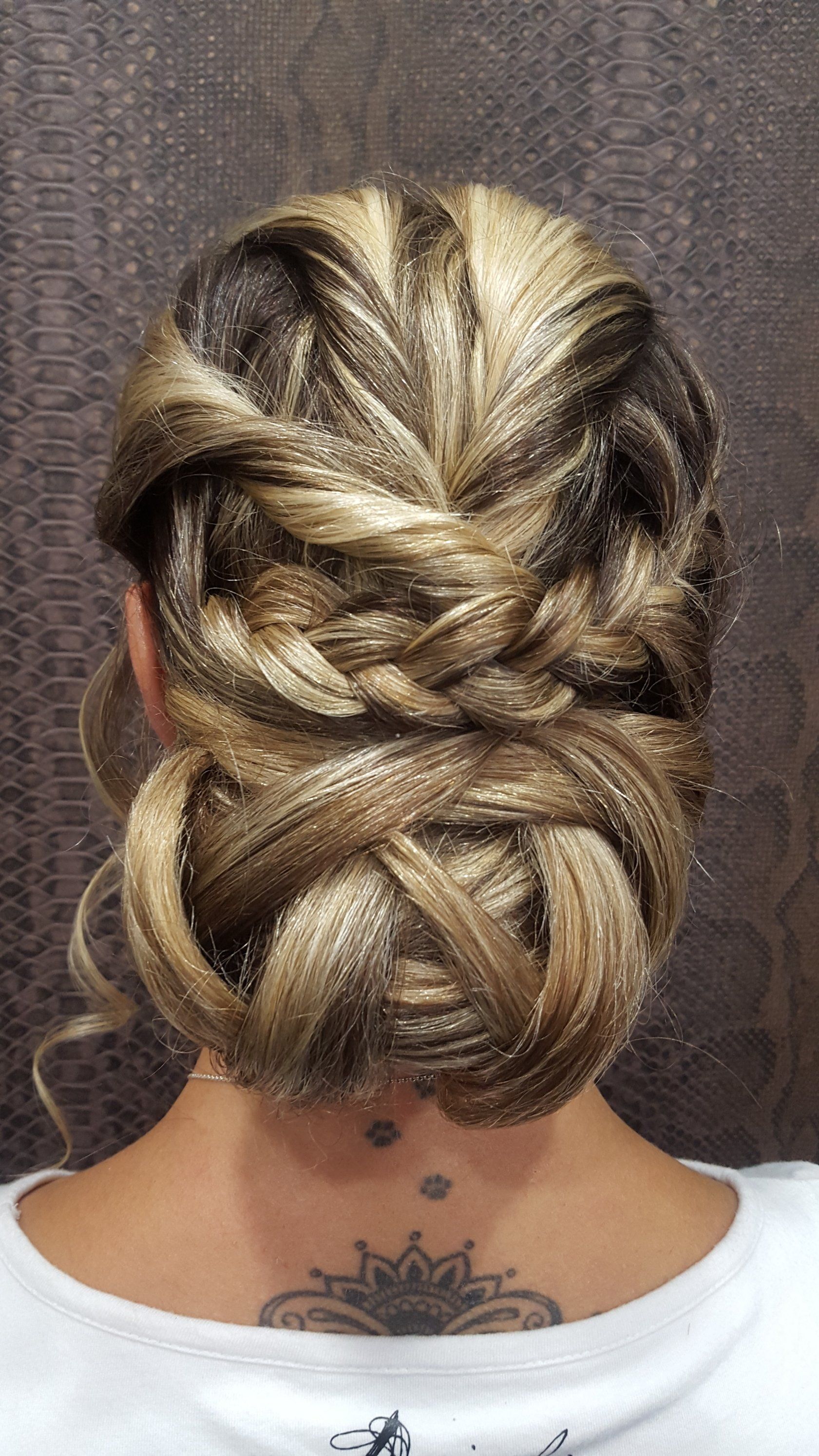 La parte posterior de la cabeza de una mujer con un moño trenzado y un tatuaje en el cuello.