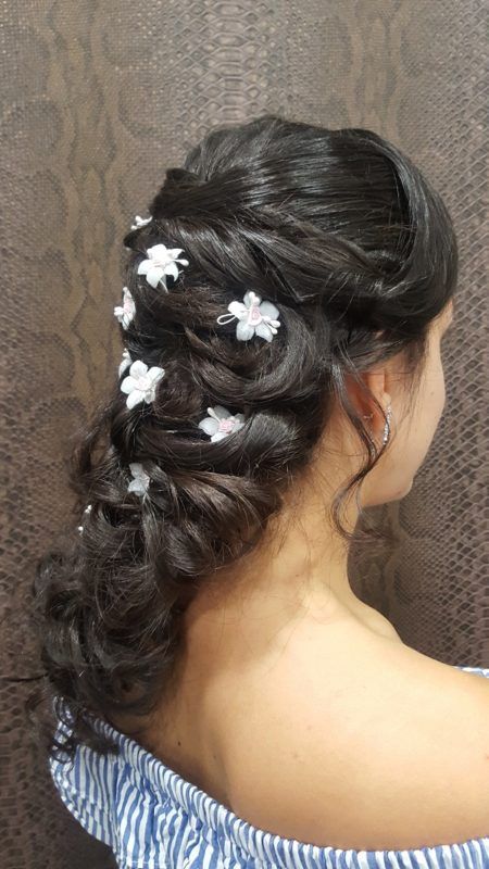 Una mujer lleva un peinado trenzado con flores blancas en el cabello.