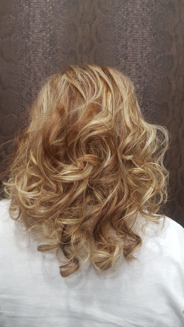 Una mujer con cabello rubio y rizado lleva una camisa blanca.