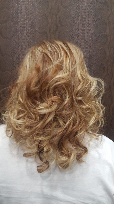 Una mujer con cabello rubio y rizado lleva una camisa blanca.