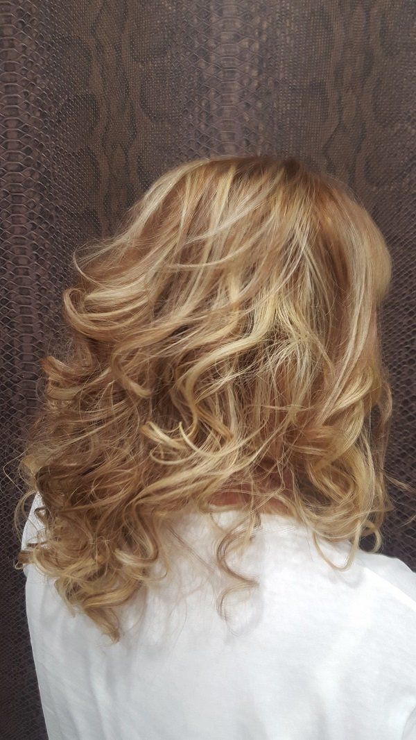 Una mujer con cabello rubio y rizado lleva una camisa blanca.