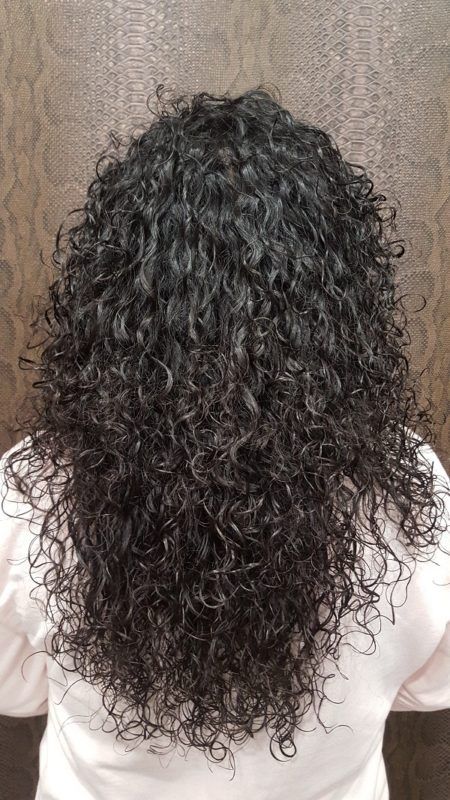 Una mujer con cabello largo y rizado está parada frente a una pared de madera.