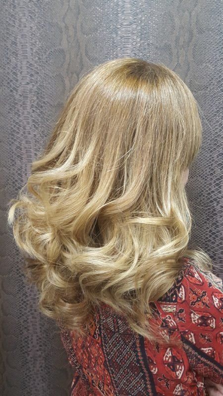 Una mujer con cabello largo y rubio está parada frente a una pared.