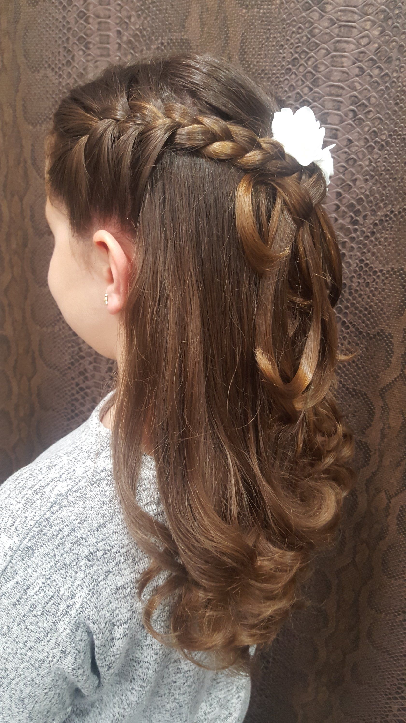 Una niña lleva un peinado trenzado con una flor en el pelo.