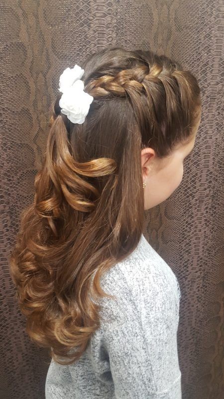 Una niña lleva una cola de caballo trenzada con una flor en el pelo.