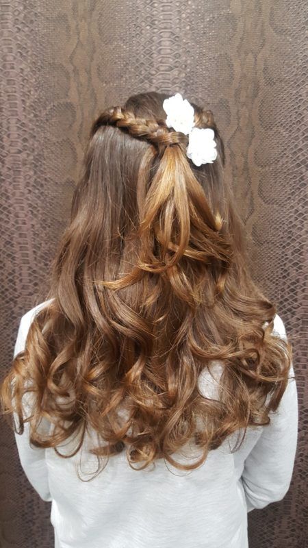 Una niña lleva un peinado mitad recogido mitad suelto con una flor en el pelo.