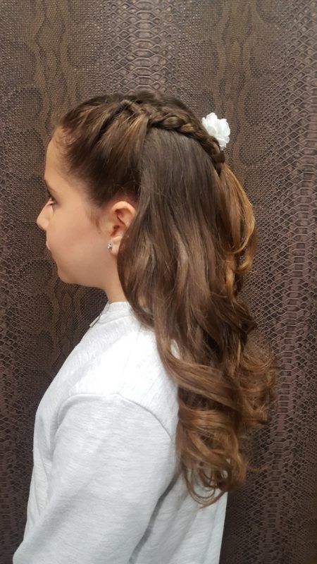 Una niña lleva una cola de caballo trenzada con una flor en el pelo.