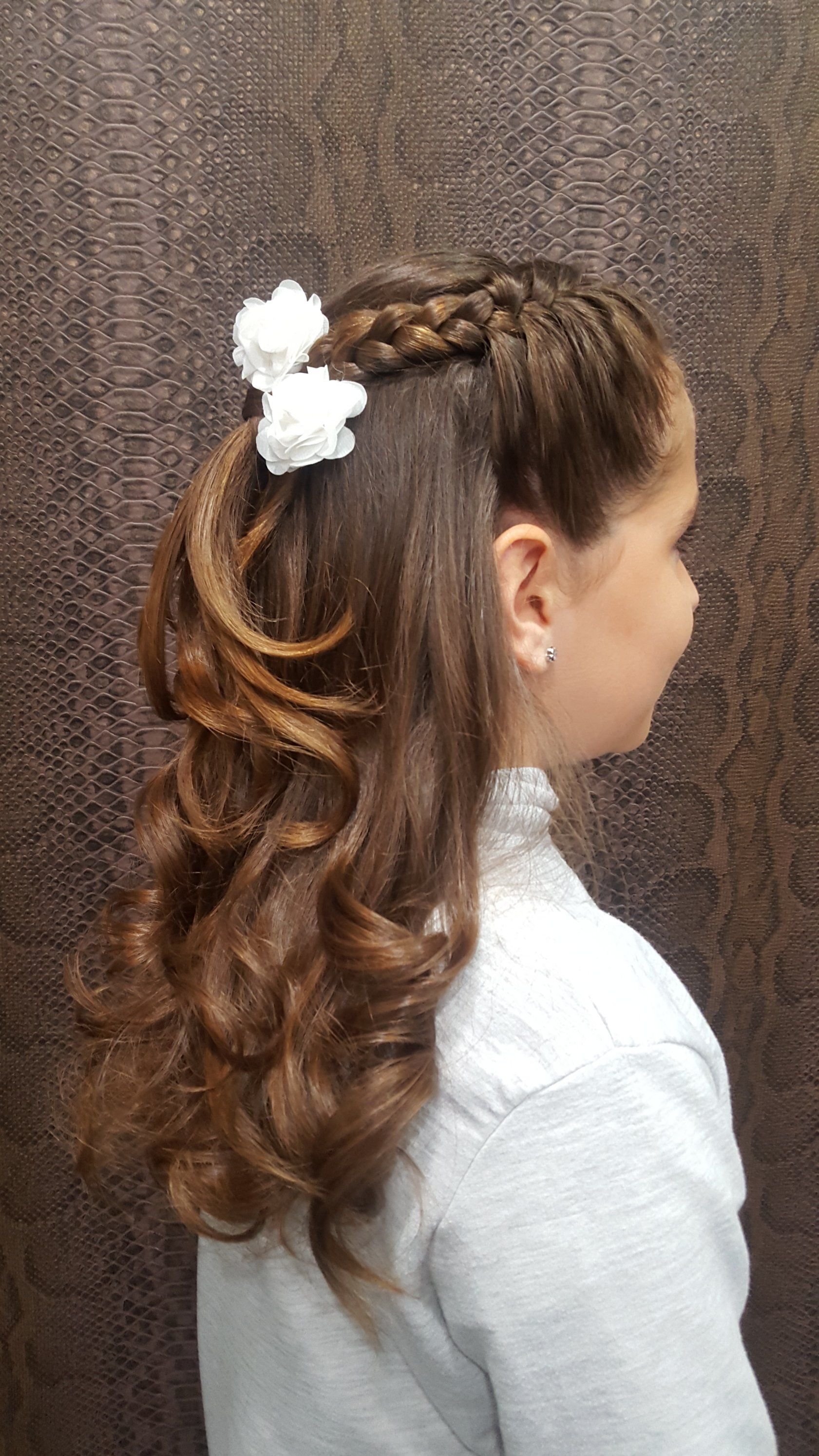 Una niña lleva un peinado trenzado con una flor en el pelo.